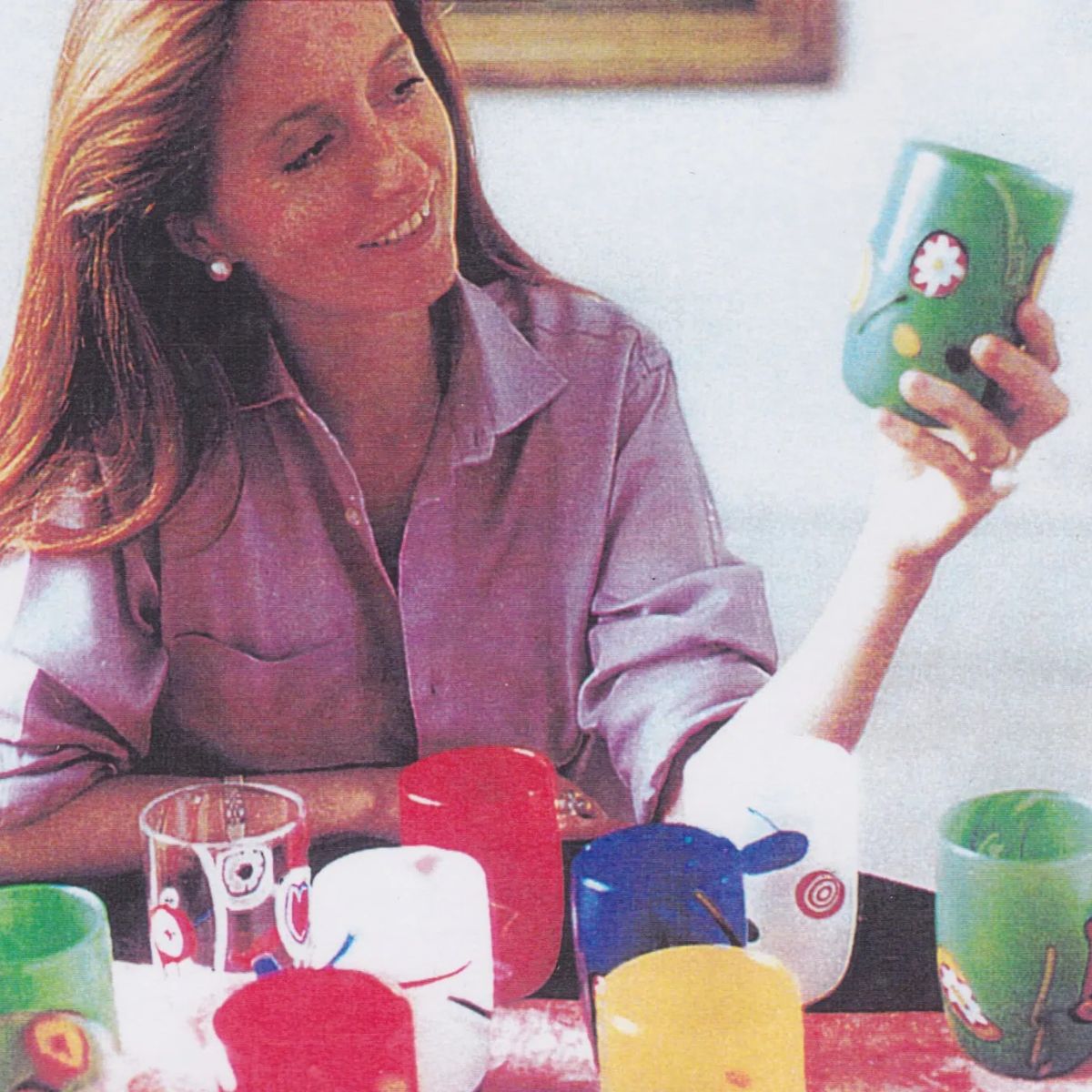 Marie Brandolini, holding and inspecting a colorful green hand blown glass cup.