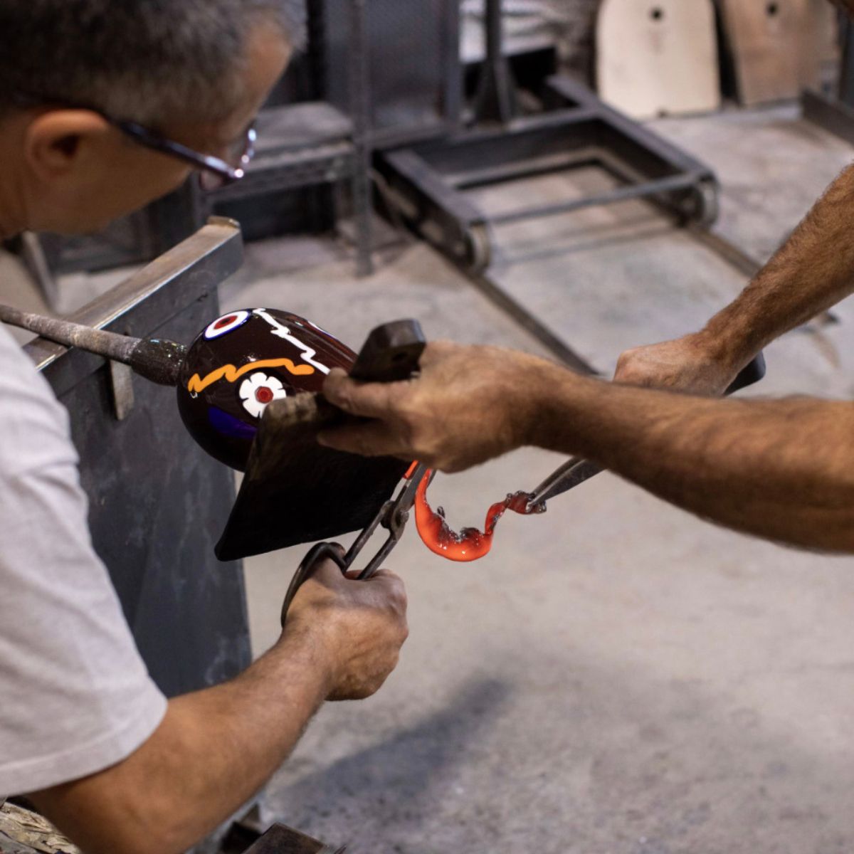 Craftsman working on a hand blown glass fresh out of the oven.