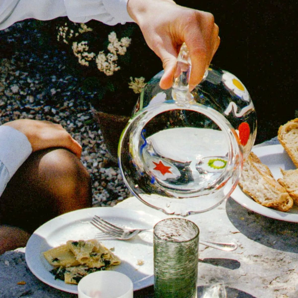 Womans hand at a picnic pouring water into a green glass from a murano glass pitcher.